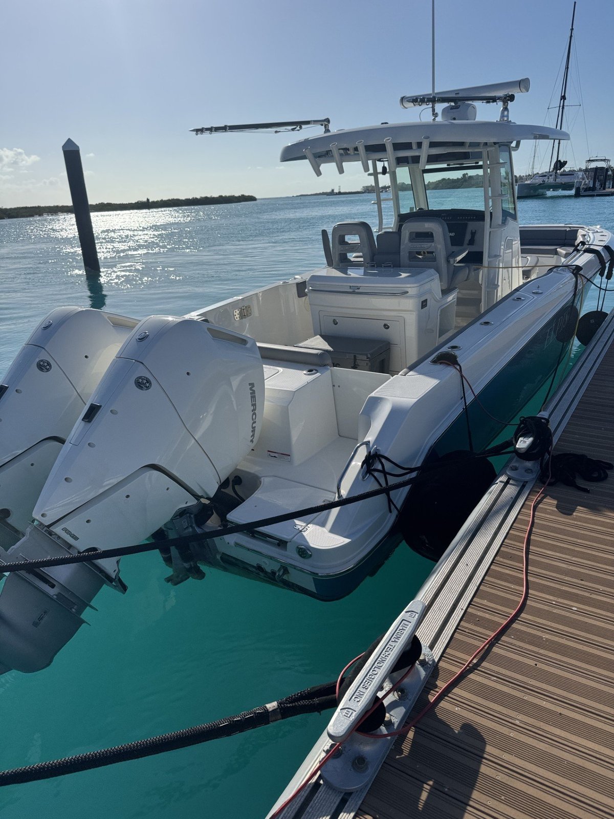White center console fishing boat docked at a wooden marina with turquoise water
