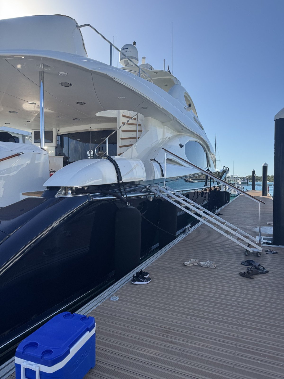 Large white luxury yacht docked at marina with tender boat, mooring lines, and wooden dock